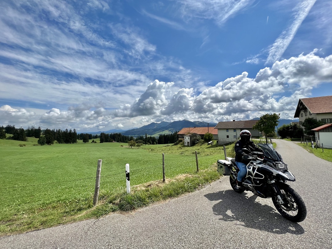 BMW Motorradfahrer auf alpiner Landstraße – weite Berge und blauer Himmel