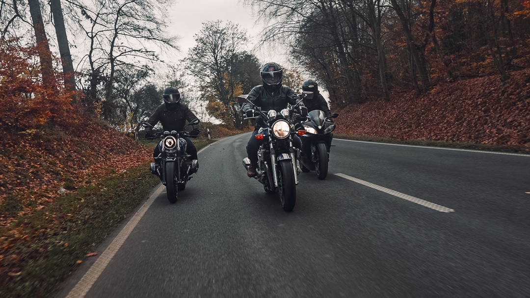 Drei Motorradfahrer fahren gemeinsam auf kurviger Herbststraße